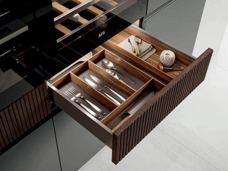 Närbild på utdragbar kökslåda med bestickinredning och en köksfront i ribbat trä.